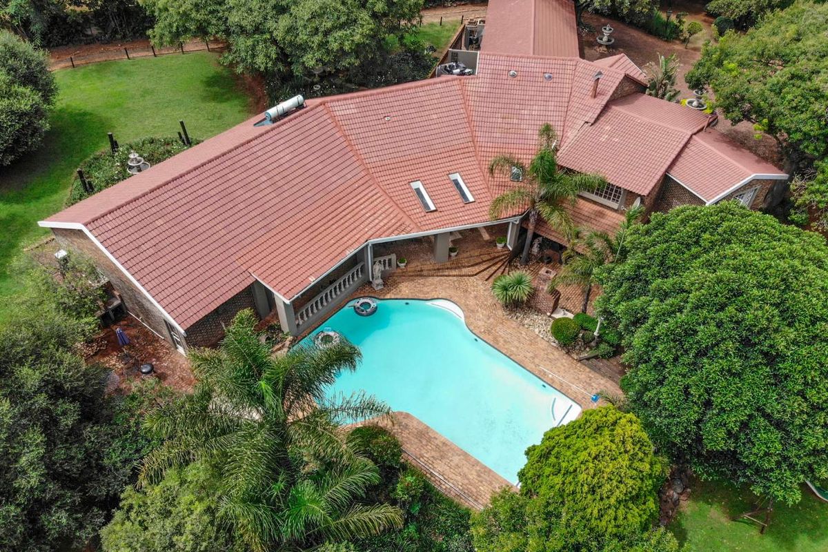 Aerial view of a residential property featuring a large swimming pool, expansive garden, and a tiled roof structure with skylights.