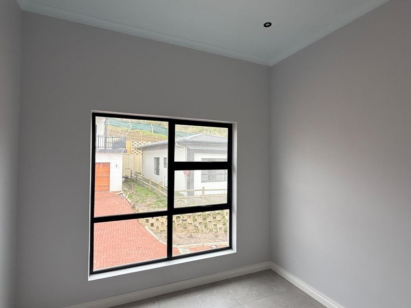 A bright, empty bedroom featuring modern tiled flooring, neutral walls, and a large black-framed window providing natural light and a view of the exterior.