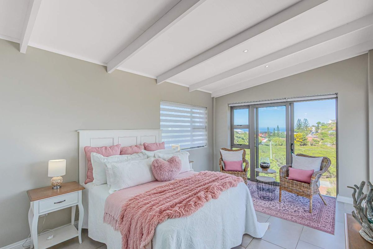 Bright bedroom featuring exposed ceiling beams, tiled flooring, and large sliding glass doors opening to a scenic coastal view.