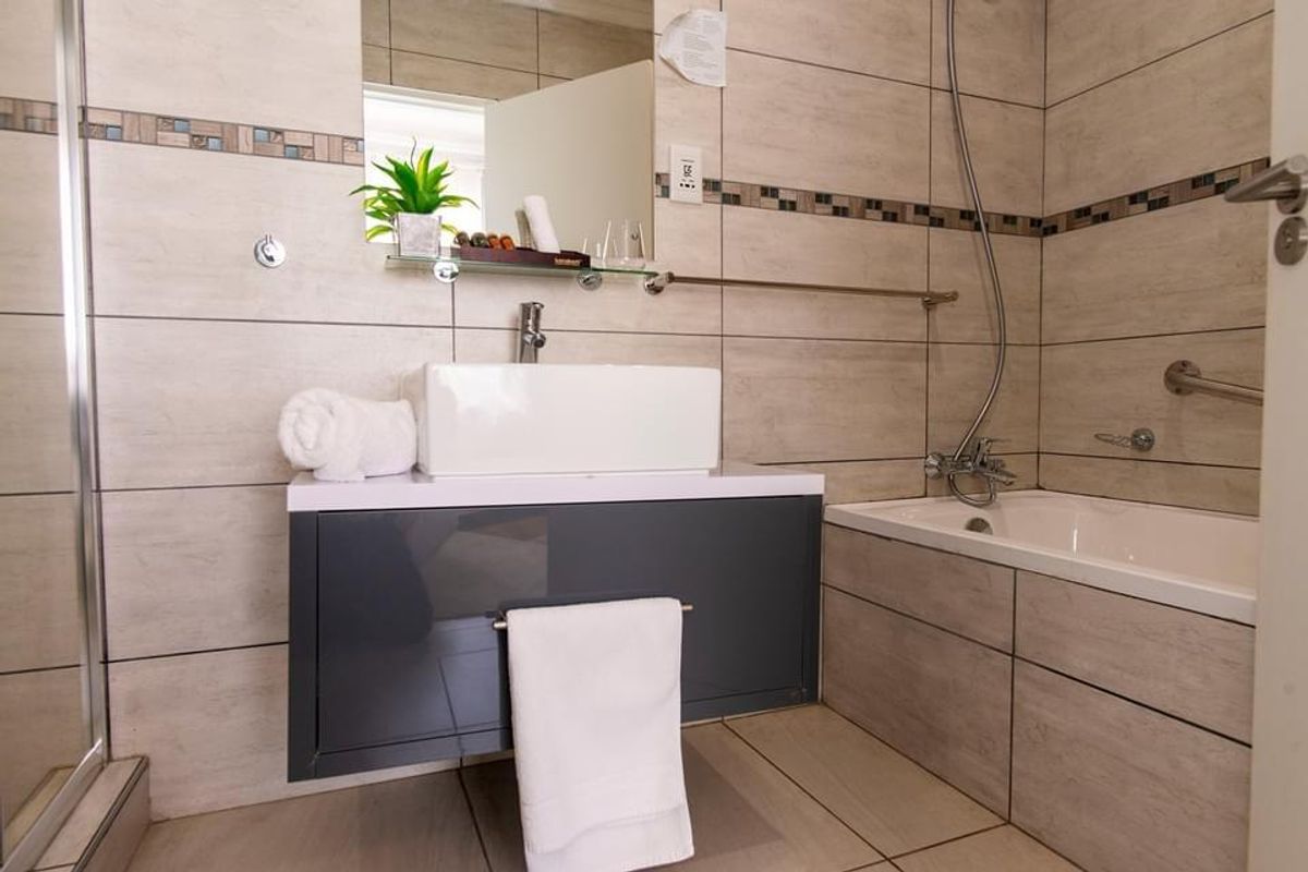 A modern hotel bathroom featuring a wall-mounted vanity with a vessel sink, a bathtub with a handheld shower attachment, and neutral wall tiling.