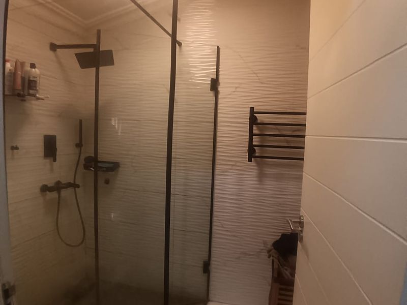 Modern bathroom featuring a walk-in shower with black fixtures, textured wall tiling, and a heated towel rail.