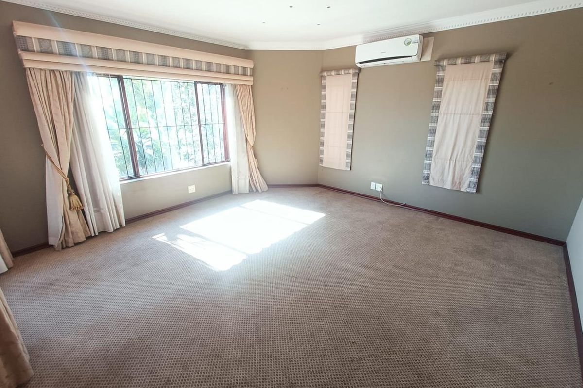 Spacious bedroom featuring neutral wall tones, wall-mounted air conditioning unit, and large windows with integrated security bars.
