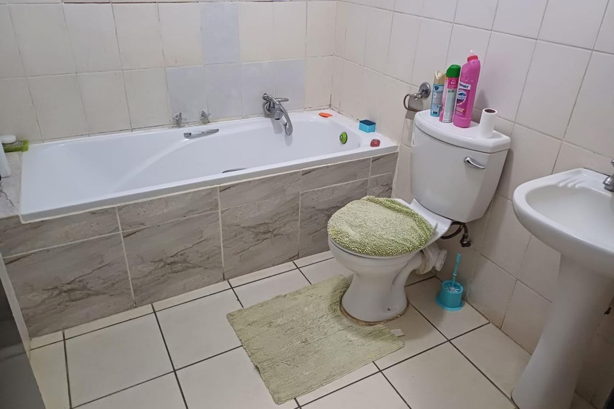 A functional bathroom featuring a built-in bathtub with tiled surround, a standard pedestal basin, and a toilet.