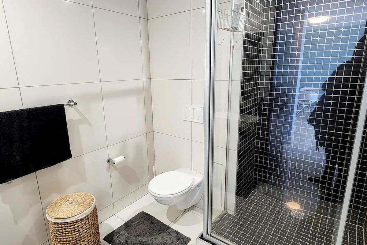 Modern bathroom featuring a glass-enclosed shower with black mosaic tiling, a wall-mounted toilet, and large-format white wall tiles.