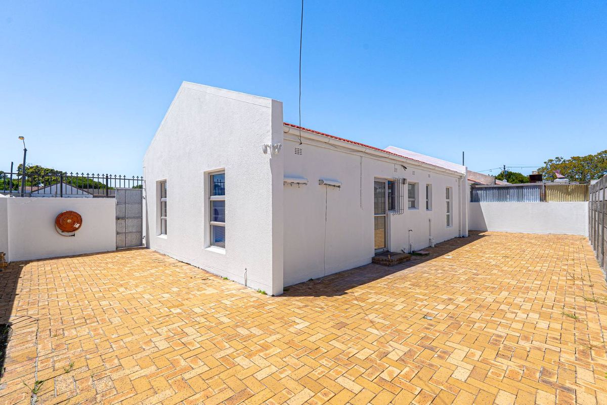 A rear exterior view of the property featuring a paved courtyard, white rendered walls, and a tiled roof.