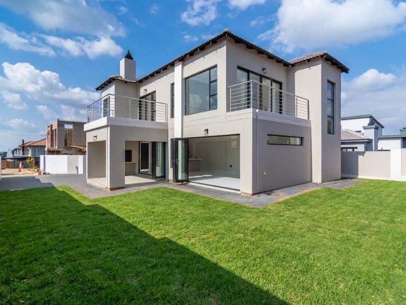 Modern double-story rear elevation featuring a spacious lawn, covered patio with built-in braai, and an upper-level balcony with stainless steel balustrades.