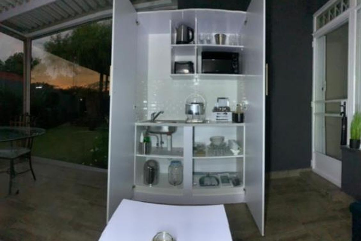 A compact, built-in kitchenette unit featuring a sink, tiled backsplash, and integrated shelving, located within a covered patio area.