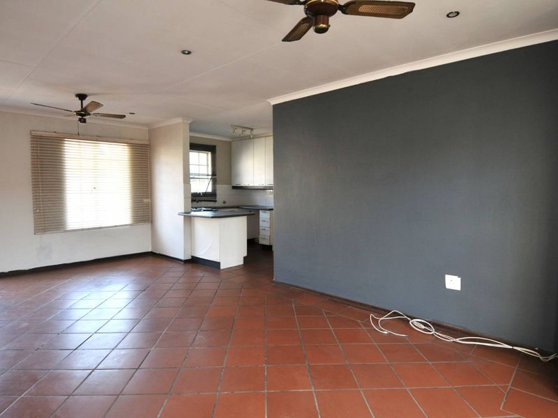 Spacious open-plan living area featuring terracotta floor tiles, ceiling fans, and an adjoining kitchen with built-in cabinetry.