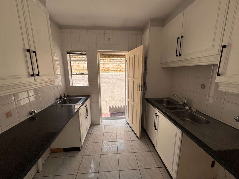 A functional galley-style kitchen featuring ample built-in cabinetry, granite countertops, dual sink areas, and direct access to an exterior courtyard.