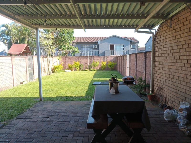 A covered patio area with brick paving, featuring a corrugated metal roof structure overlooking a private enclosed garden with brick boundary walls.