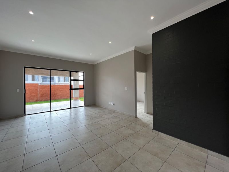 Spacious, empty living area featuring neutral tiled floors, a striking black feature brick wall, recessed lighting, and large sliding doors opening to the patio.