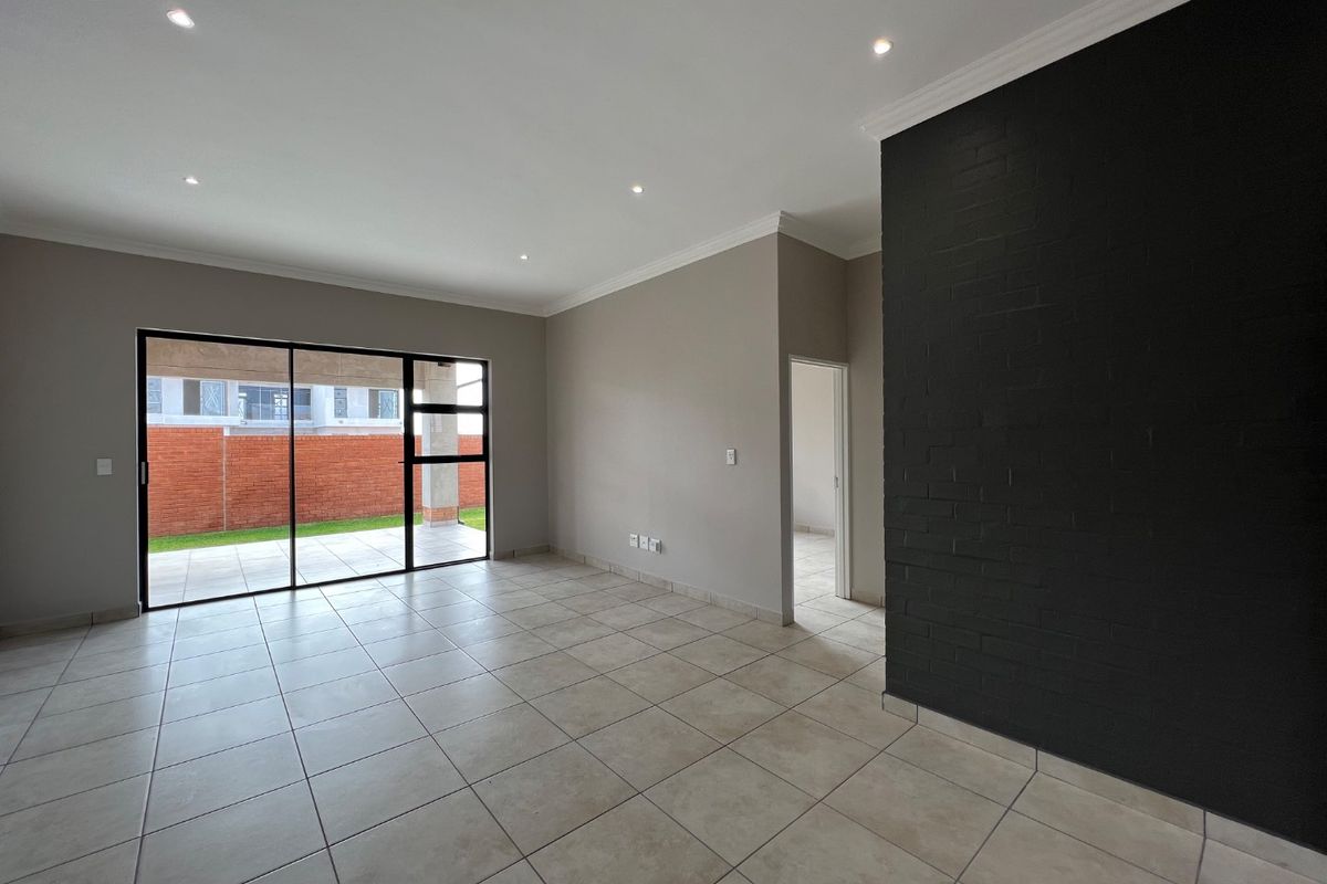 Spacious, empty living area featuring neutral tiled floors, a striking black feature brick wall, recessed lighting, and large sliding doors opening to the patio.