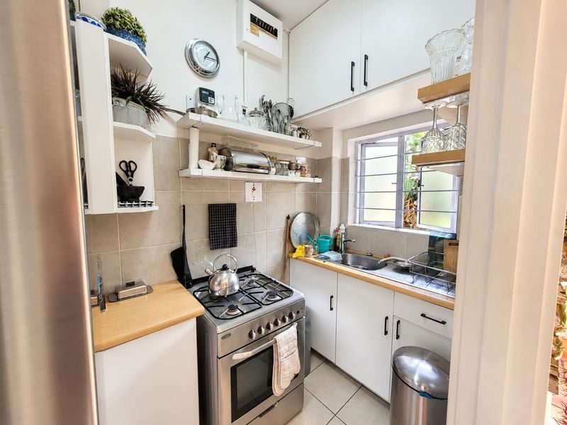 Compact kitchen featuring a gas stove, stainless steel sink, tiled backsplash, and ample built-in cabinetry with open shelving for storage.