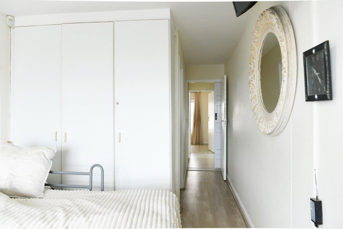 A bedroom featuring built-in floor-to-ceiling wardrobes and light-toned flooring, with a hallway leading to an adjacent room.