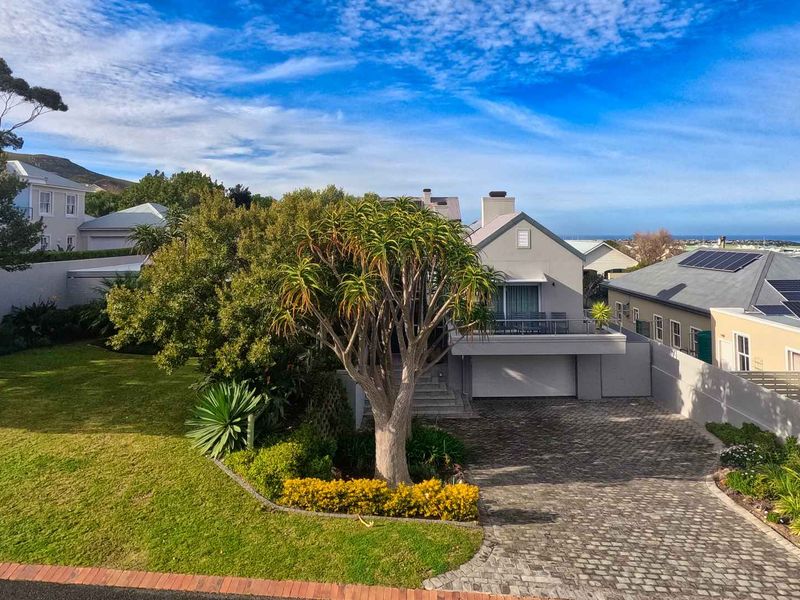 Elevated view of a well-maintained residential property featuring a paved driveway, landscaped garden, double garage, and an upper-level balcony.