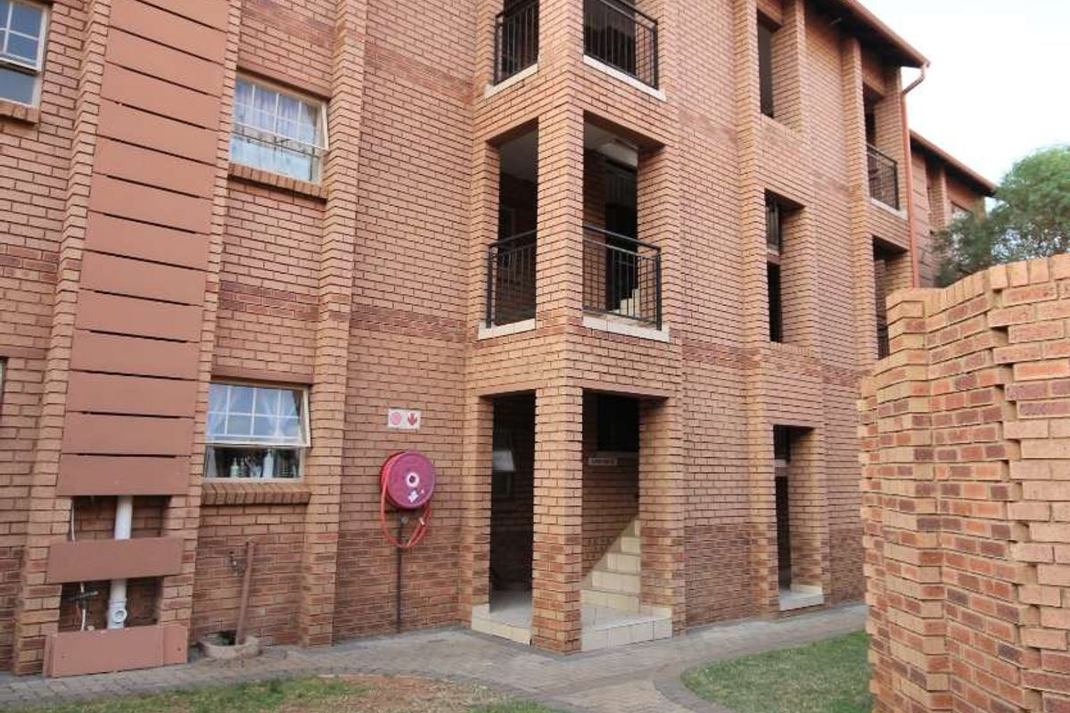 Exterior view of a multi-story apartment building featuring face brick construction, private balconies with metal railings, and a paved walkway through the garden area.