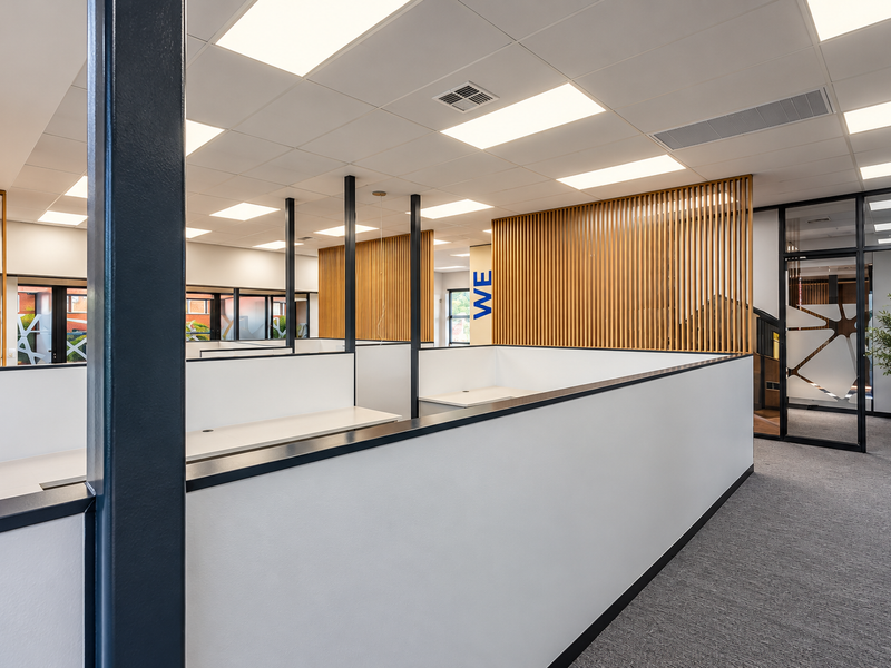 Modern open-plan office space featuring contemporary timber slat dividers, glass partitions, suspended ceilings, and high-quality carpet flooring.