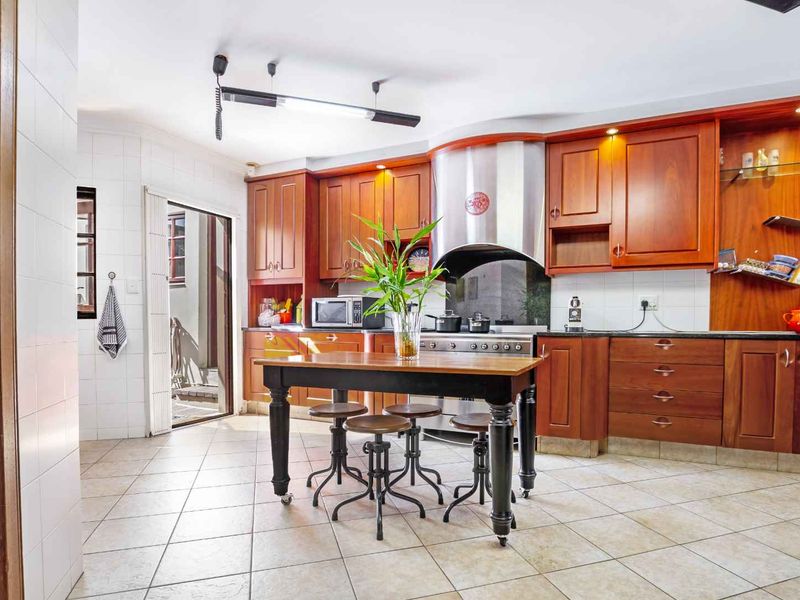A functional kitchen featuring warm-toned wooden cabinetry, granite countertops, a stainless steel extractor fan, and tiled flooring with direct access to an outdoor area.