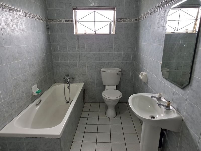 A functional bathroom featuring a bathtub, pedestal sink, and toilet, finished with full-height wall tiling and floor tiles.