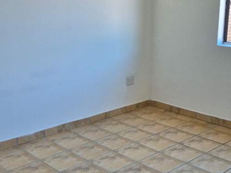 An empty bedroom featuring neutral tiled flooring and plain white walls, providing a blank canvas for interior design.