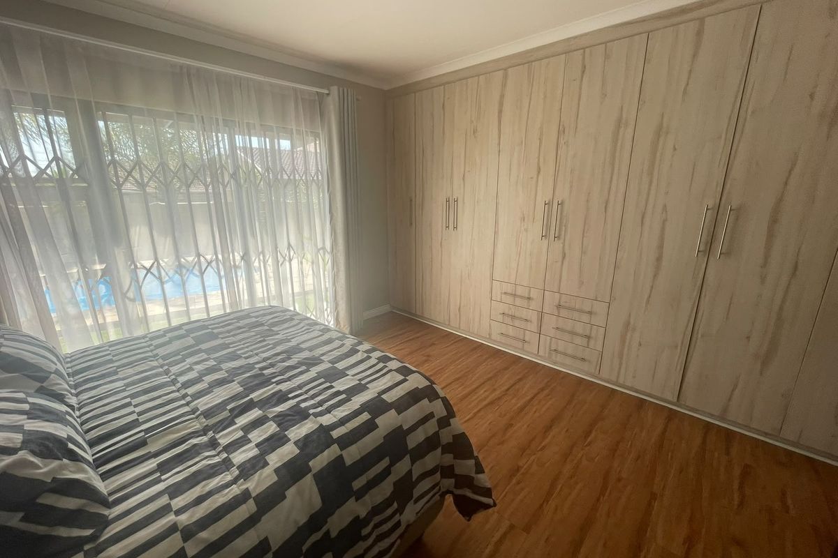 Spacious bedroom featuring light wood-grain built-in cupboards, warm laminate flooring, and a sliding door providing access to the outdoor pool area.