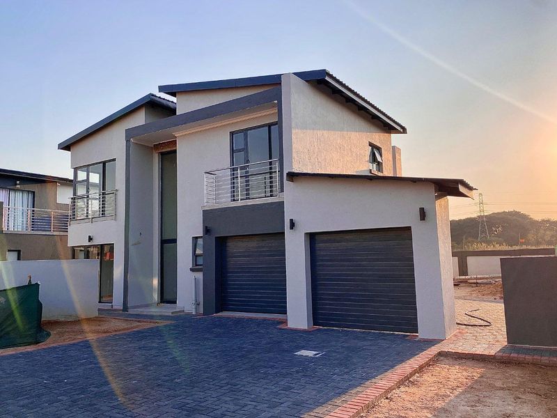 Modern double-story residential home featuring a double garage, paved driveway, and upper-level balconies with stainless steel railings.