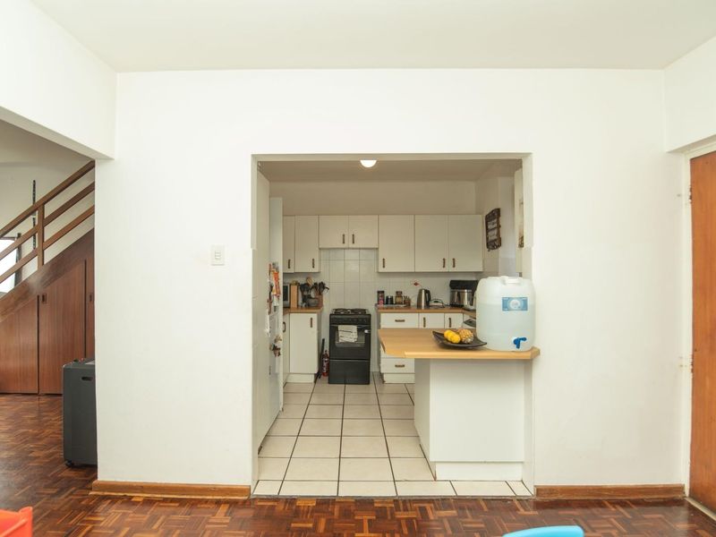 A functional kitchen featuring white cabinetry, tiled flooring, and a timber breakfast bar, opening into a living area with parquet flooring.