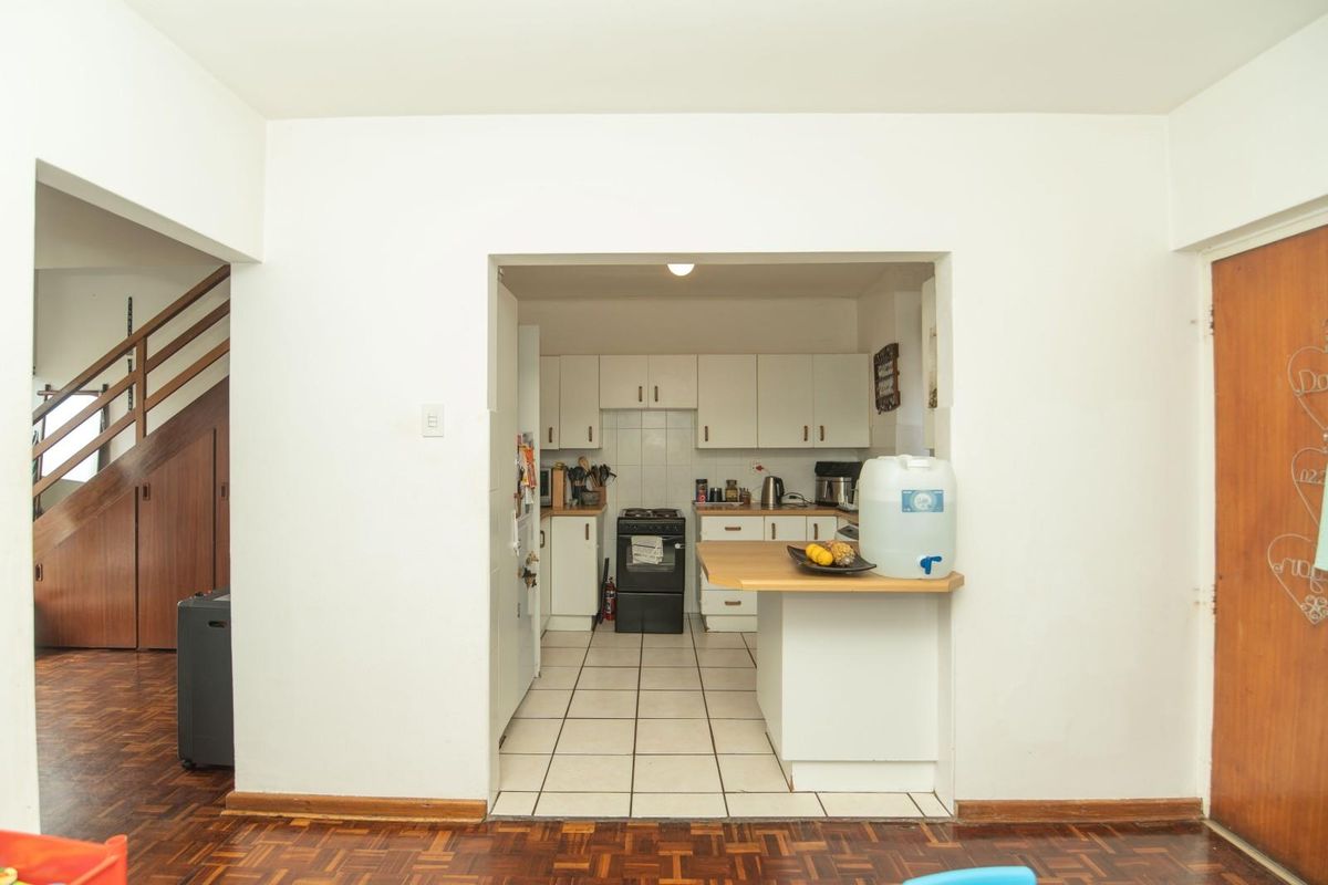 A functional kitchen featuring white cabinetry, tiled flooring, and a timber breakfast bar, opening into a living area with parquet flooring.