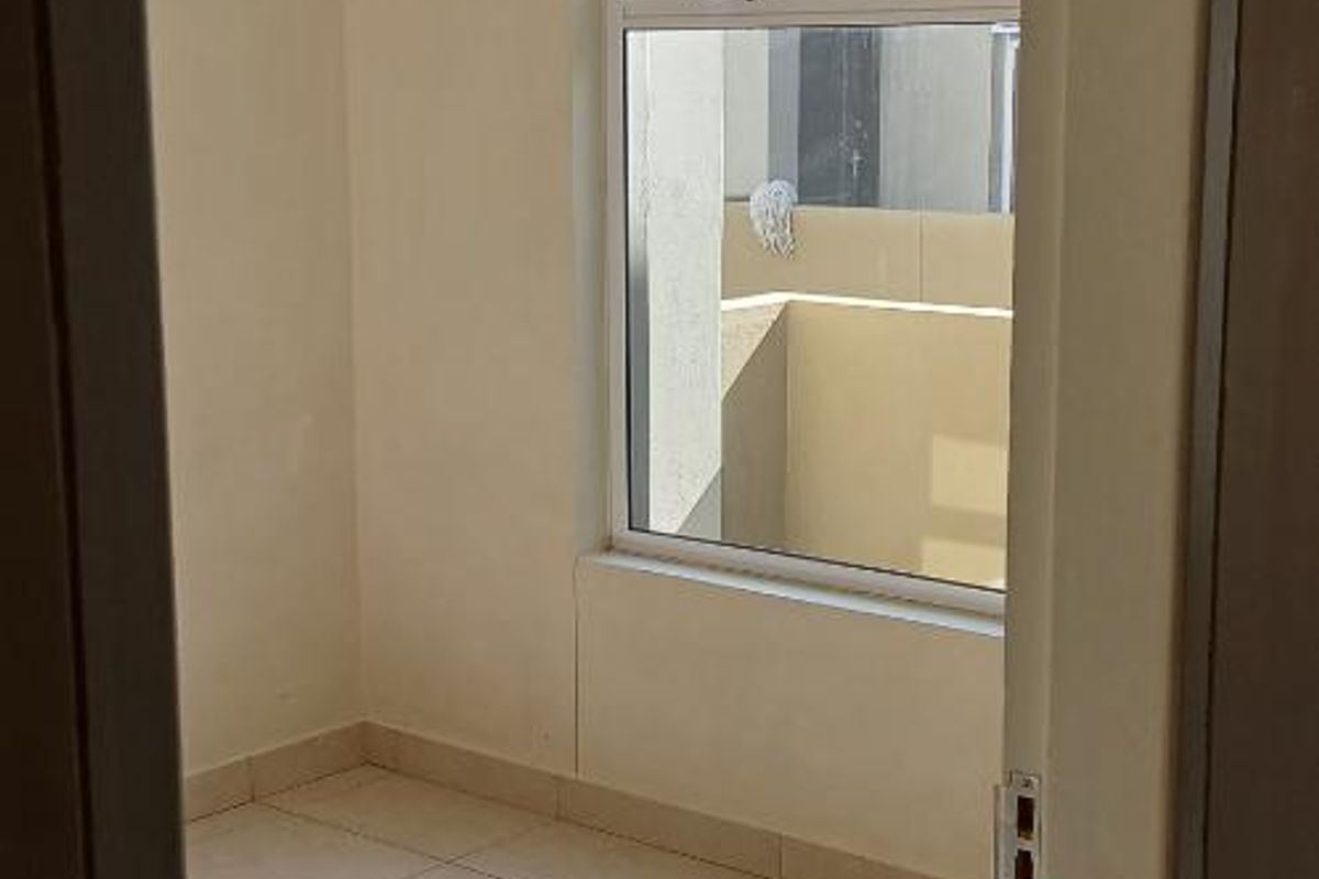 A bright, empty bedroom featuring neutral tiled flooring and a large window, providing a clean and versatile space ready for personalization.