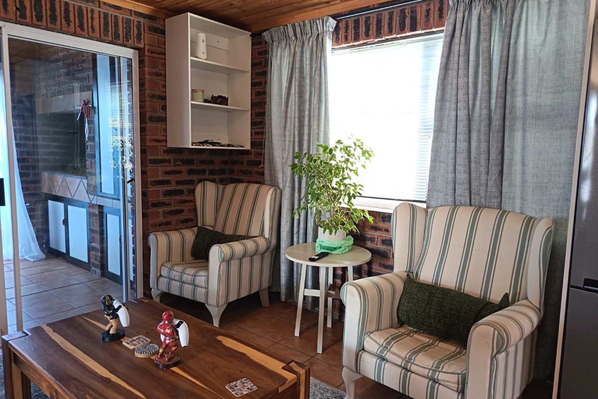 A cozy living area featuring exposed brick walls, a warm timber ceiling, tiled floors, and direct access to an outdoor patio through sliding glass doors.