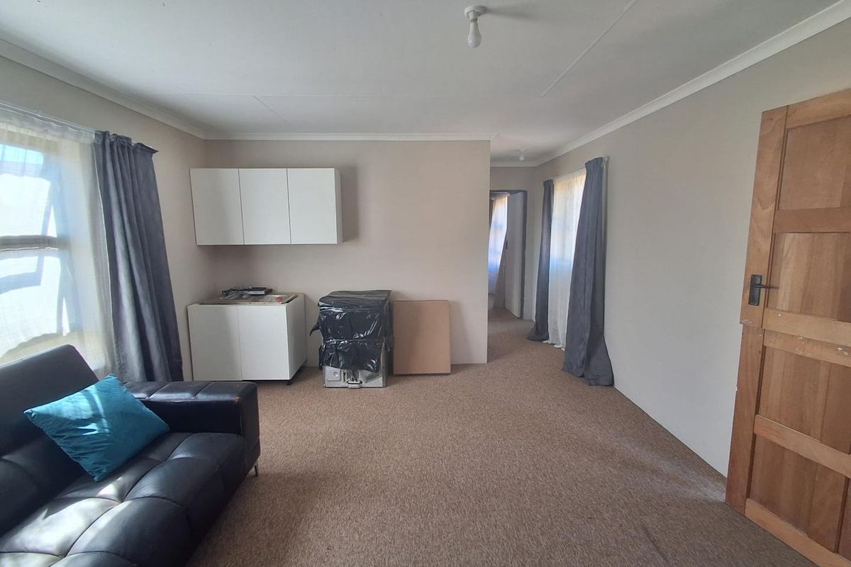 A living room featuring carpeted flooring, built-in wall cabinetry, and a timber door, offering a functional space with potential for cosmetic updates.