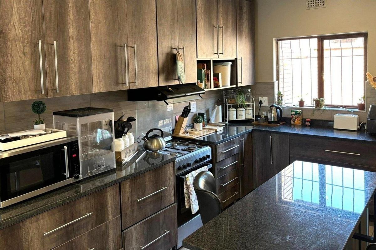 Modern kitchen featuring dark wood cabinetry, granite countertops, a central island, and a gas stove with an extractor fan.