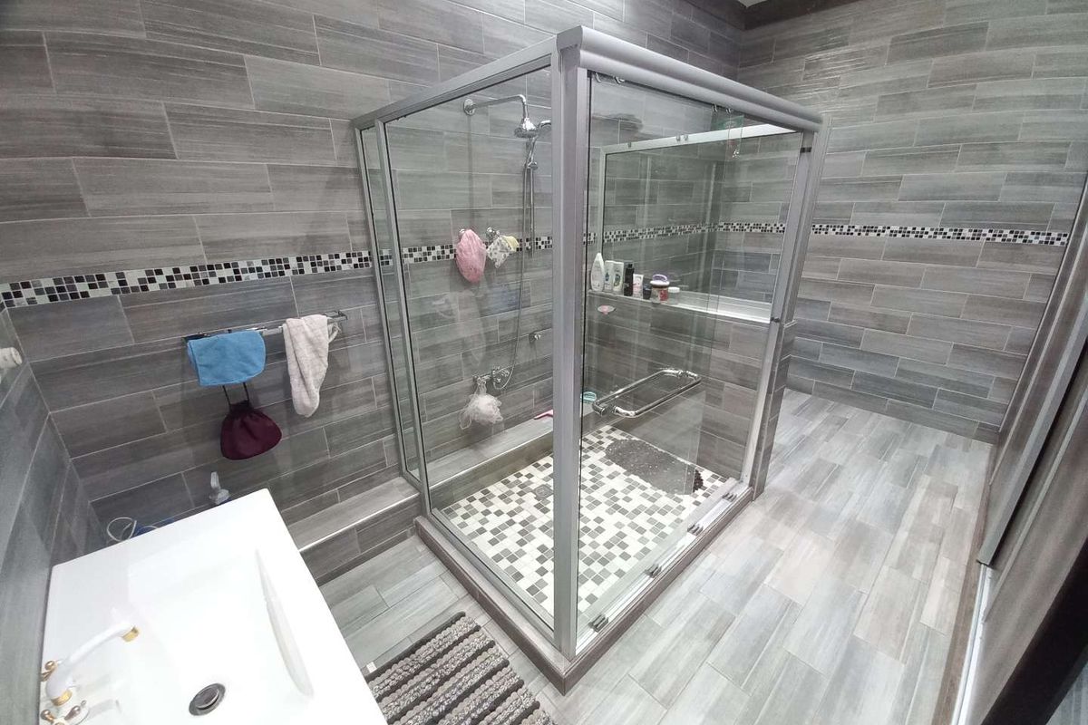 Modern bathroom featuring a glass-enclosed walk-in shower with mosaic tile flooring, grey wall tiling, and a contemporary vanity basin.