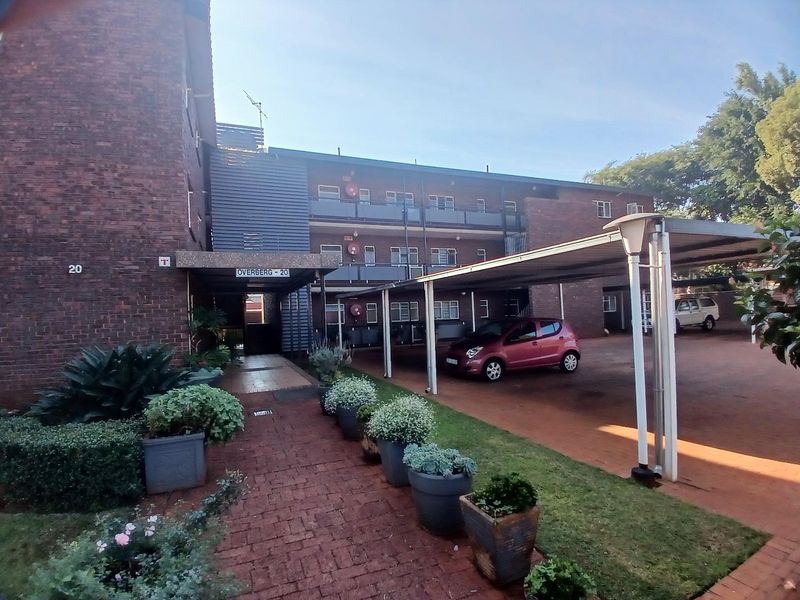 Exterior view of the Overberg apartment complex featuring a brick facade, covered parking carports, and a paved entrance walkway.
