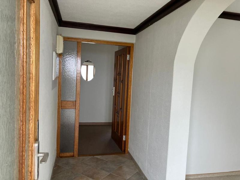 A bright entrance hall featuring classic timber door frames, textured glass detailing, and an arched transition leading into the main living area.