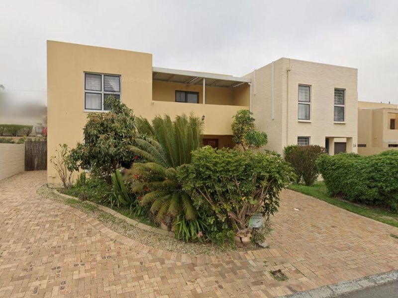 Front elevation of a two-story residential property featuring a paved driveway, landscaped garden area, and an upper-level balcony.