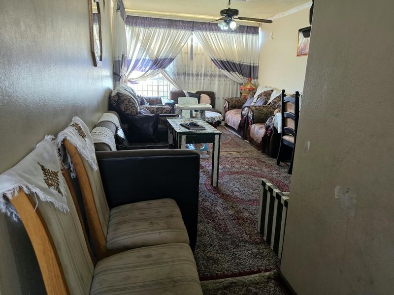 A living room area featuring a ceiling fan and window curtain rails, showing signs of wear on the wall surfaces.