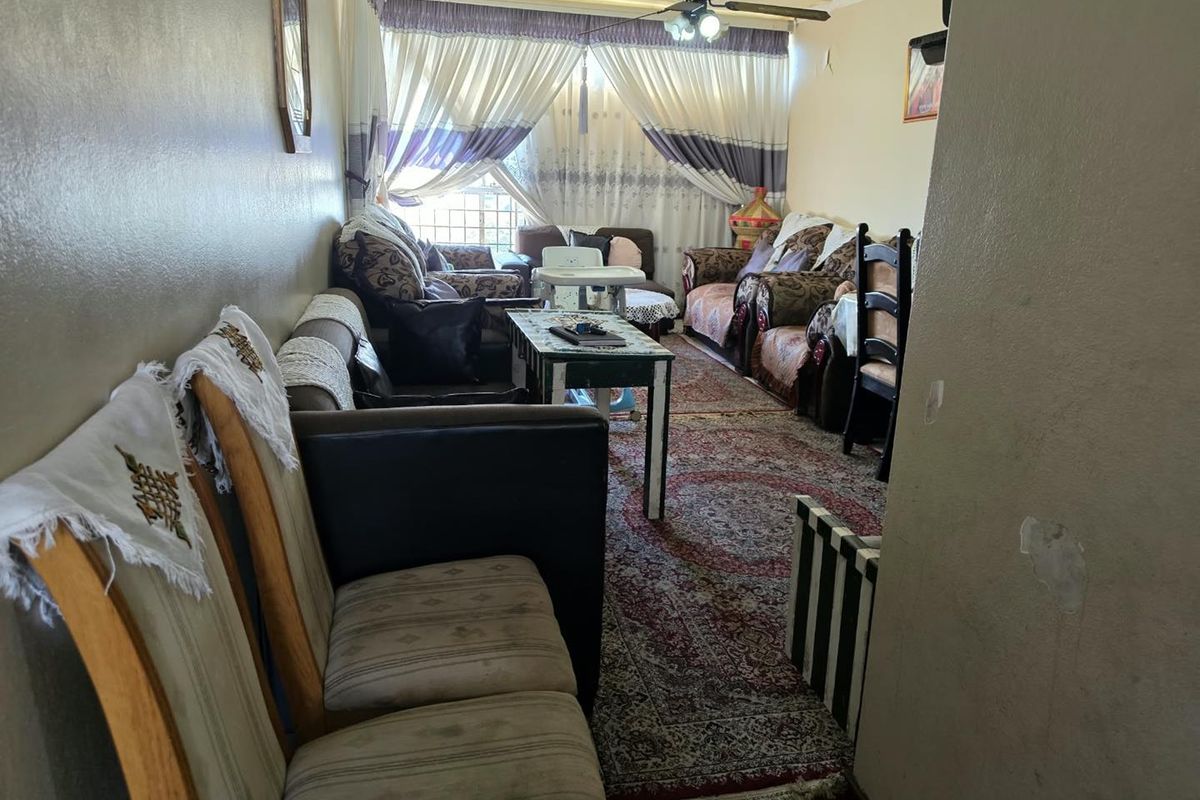 A living room area featuring a ceiling fan and window curtain rails, showing signs of wear on the wall surfaces.