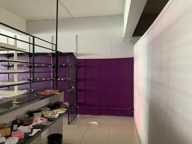 Retail space featuring tiled flooring, built-in metal shelving units, and a security gate, currently requiring cosmetic updates and maintenance.