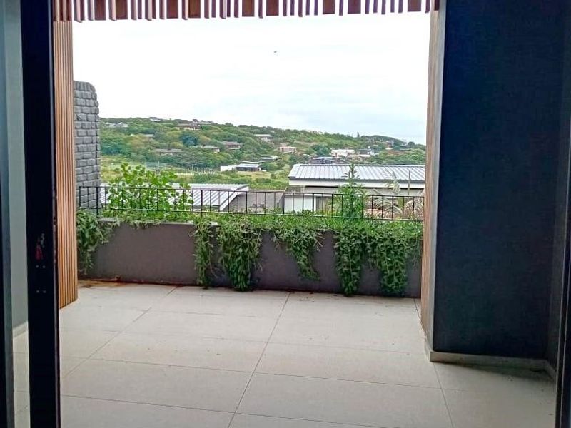 A covered balcony featuring tiled flooring, a metal balustrade, and a built-in planter box, offering elevated views of the surrounding landscape.