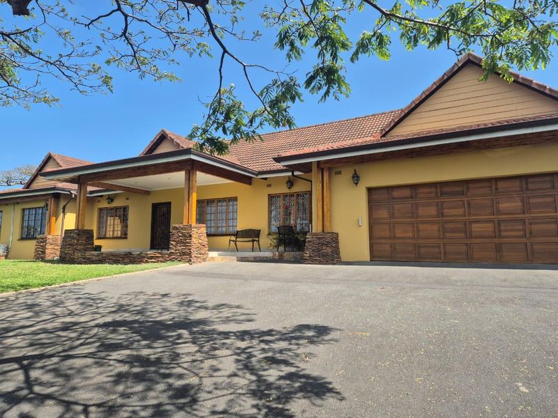 A well-maintained single-story residence featuring a tiled roof, stone-clad entrance pillars, timber beams, and an integrated double garage with a paved driveway.
