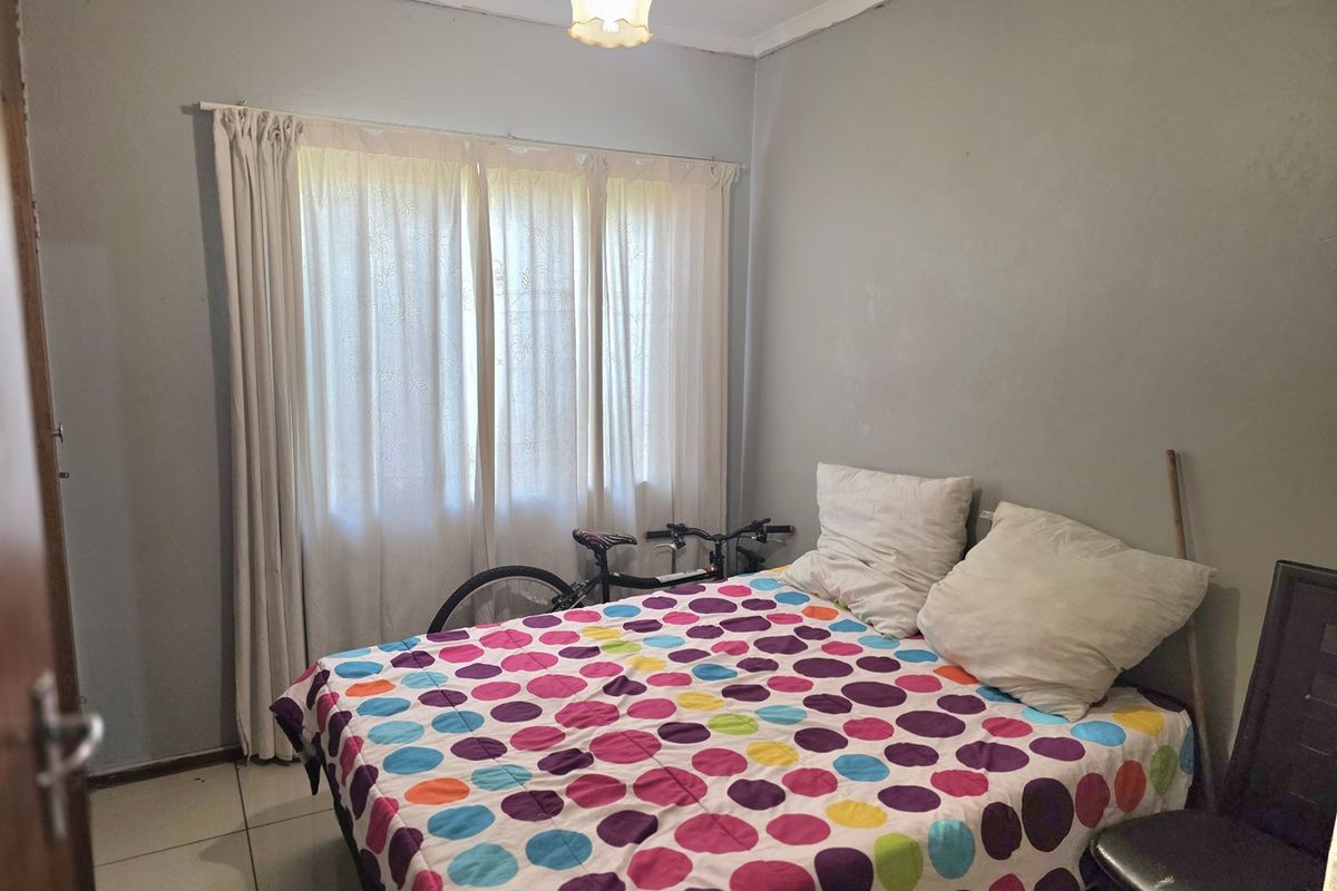 A functional bedroom featuring tiled flooring, neutral wall paint, and a window with curtain treatments.