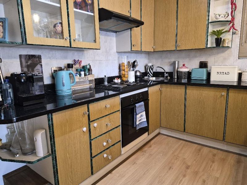 A functional kitchen featuring wood-look laminate cabinetry, black granite countertops, a built-in oven, and an extractor fan with a tiled backsplash.