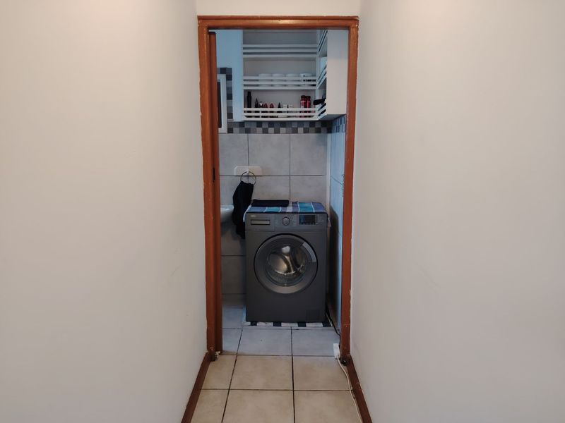 A functional laundry area featuring tiled walls and flooring with built-in shelving, accessible through a wooden door frame.