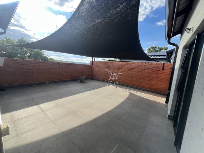 Spacious outdoor patio area featuring tiled flooring, a brick boundary wall, and a large overhead shade sail for sun protection.