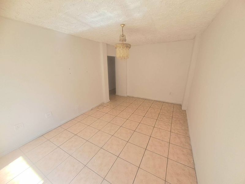 An empty living room featuring ceramic tile flooring, a textured ceiling, and a central pendant light fixture, ready for renovation or staging.