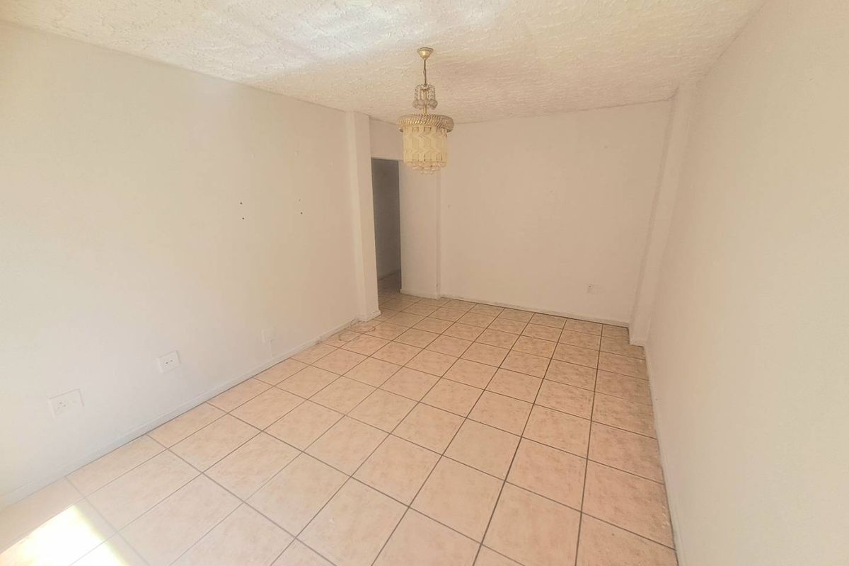 An empty living room featuring ceramic tile flooring, a textured ceiling, and a central pendant light fixture, ready for renovation or staging.