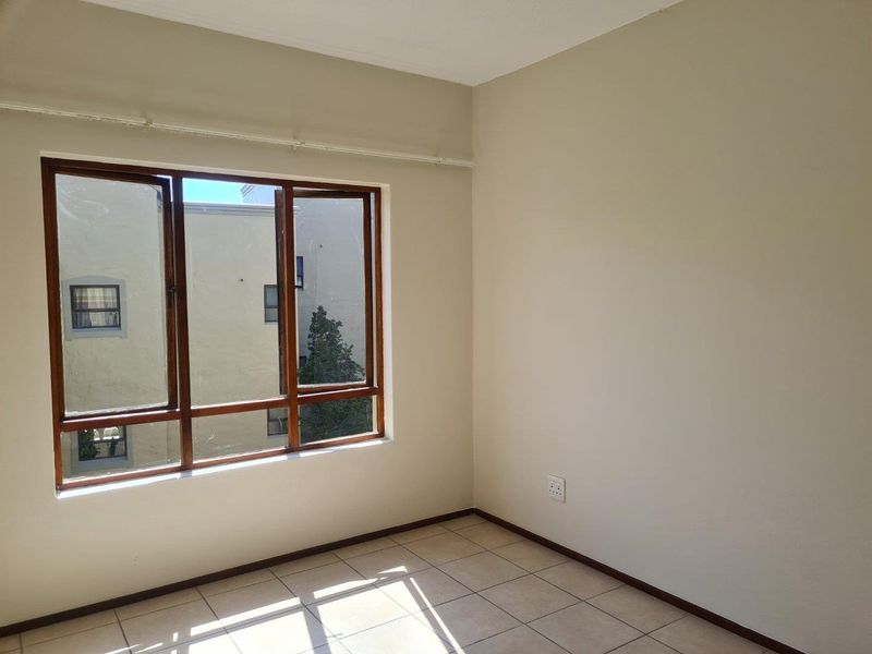 A bright, empty bedroom featuring neutral walls, ceramic tiled flooring, and large timber-framed windows providing natural light.
