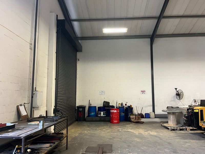 Industrial utility space featuring high ceilings with exposed steel beams, concrete flooring, and a large roller shutter door for easy access.