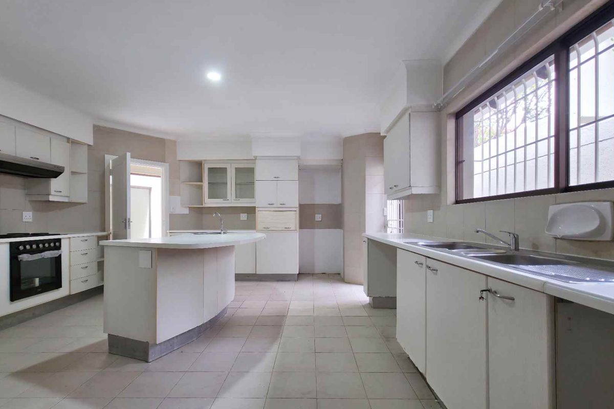 Spacious kitchen featuring white cabinetry, a central island, built-in oven, extractor fan, and double basin sink with tiled flooring.